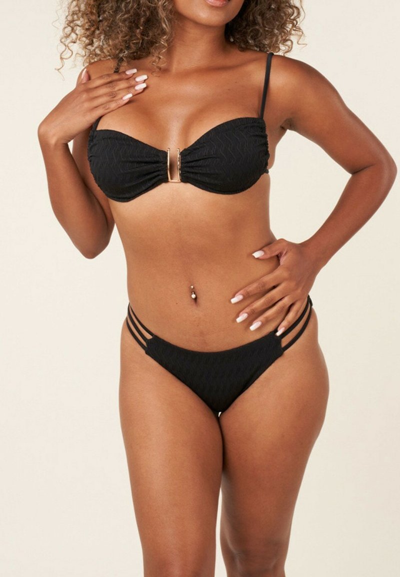 Ensemble bikini noir avec un haut bandeau texturé décoré d'un accent doré et un bas taille basse avec plusieurs lanières sur les côtés.