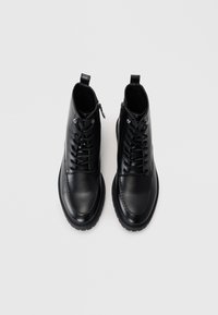 Botas de tobillo de cuero negro con punta redonda, cordones en la parte delantera, cremallera lateral y suela de goma texturizada. Acabado liso con detalles de costura.
