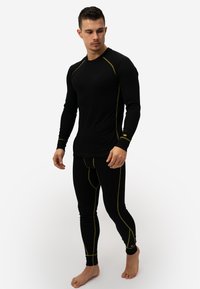 Black thermal long-sleeve top and leggings with yellow stitching. Form-fitting design; fabric appears smooth and flexible.
