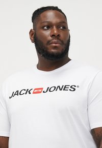Witte katoenen t-shirt met een zwart en rood "JACK & JONES" logo. Korte mouwen, ronde hals, ontspannen pasvorm en een gladde textuur.