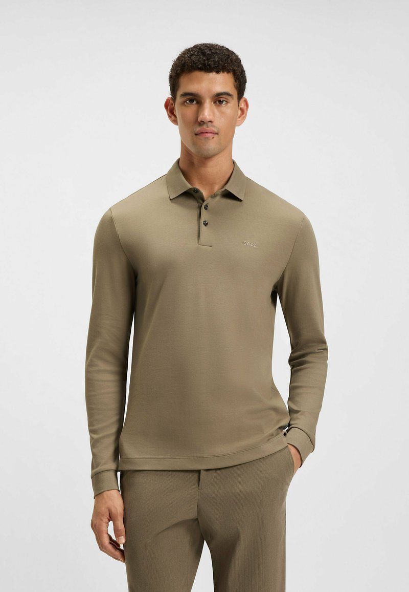 Olijfgroene polo met lange mouwen, zachte textuur, drie-knopen sluiting, subtiele logo op de borst, gecombineerd met gelijkgekleurde textuurbroek.