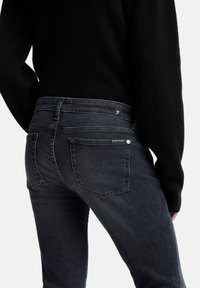 Ciemne dżinsy typu denim o dopasowanym kroju, z dwoma kieszeniami i subtelnym logo na tylnej części pasa. Miękka faktura i schludne linie.