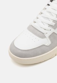 Baskets grises et blanches en matériaux en daim et en cuir. Bout arrondi, boîte à orteils perforée, détails texturés et lacets blancs plats.