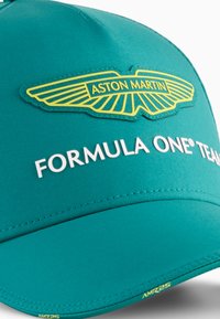 Teal kasket med en buet skygge, der har et broderet gult Aston Martin-logo og hvid tekst "FORMULA ONE® TEAM". Glat stoftekstur.