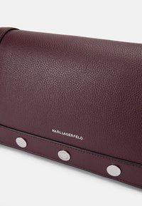 Burgunderfärgad texturerad läderväska med silverfärgade knappar och logotryck. Rektangulär form med en smakfull och minimalistisk design.