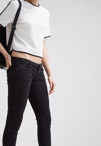 Top corto texturizado blanco con ribete negro, combinado con jeans ajustados negros. La parte superior presenta mangas cortas y un escote redondo.