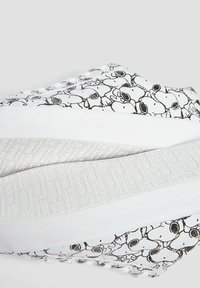 Baskets blanches avec une impression noire de Snoopy, dotées d'une semelle en caoutchouc texturée et de lacets, ainsi que d'une tige lisse et à motifs.