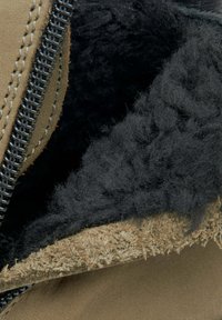 Hnědé semišové boty uvnitř s černou huňatou podšívkou, s viditelnými švy a kovovým zipem. Měkká textura s kontrastními barvami.