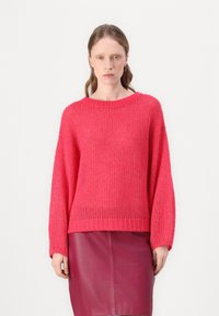 Un pull en tricot rose avec un décolleté large et de longues manches amples, associé à une jupe en cuir bordeaux. Tissu texturé avec une coupe décontractée.