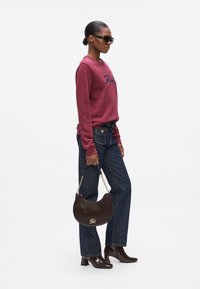 Sweatshirt bordeaux avec broderie, jean en denim foncé, un sac à main rond en cuir marron avec chaîne, et des bottes en cuir verni.