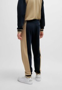 Pantaloni jogger da uomo color block in blu navy e beige, dotati di una fascia elasticizzata in vita, polsini a costine e tasche laterali, realizzati in tessuto morbido.