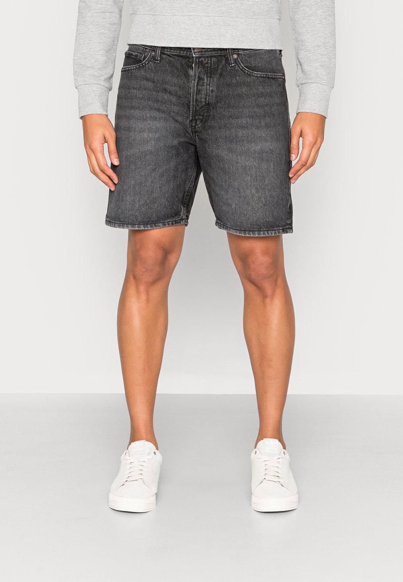 Pantalones cortos de mezclilla negra, de longitud media en el muslo, con un lavado desvaído, cinco bolsillos, detalles de costura y dobladillos enrollados, combinados con zapatillas blancas.