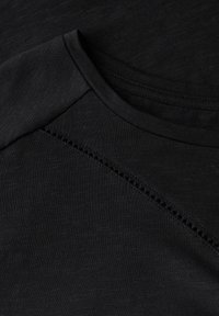 T-shirt de sport noir avec une texture lisse, un col rond et un détail de couture subtil en motif sur les épaules.