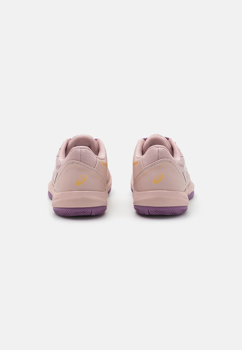 Zapatillas deportivas de color rosa claro con partes superiores de malla, suelas moradas más oscuras y detalles en amarillo. Cuentan con cuellos acolchados y superficies texturizadas.