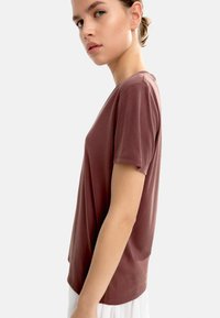 Brązowy krótki rękaw T-shirt z luźnym krojem, okrągłym dekoltem, gładką teksturą i detalami szycia, noszony z jasną spódnicą.