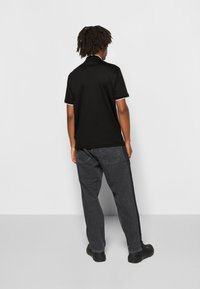 Polo noir avec bordure blanche, associé à un jean gris ample. Le tissu semble lisse avec un col classique.