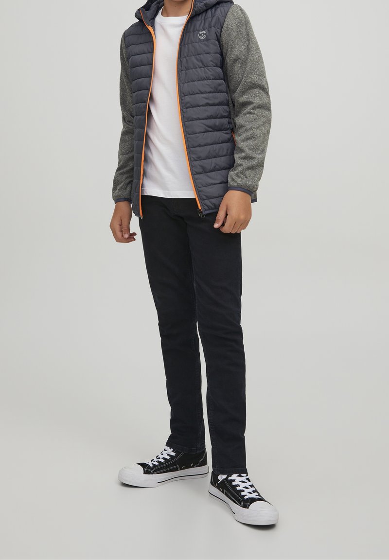 Padded dark gray jacket with orange accents, gray textured sleeves, white t-shirt, black pants, and black sneakers with white details.
