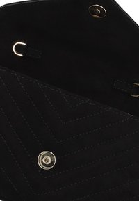 Zwarte suède tas interieur met chevron-stiksel, voorzien van een drukknoopsluiting en gouden hardware accenten.