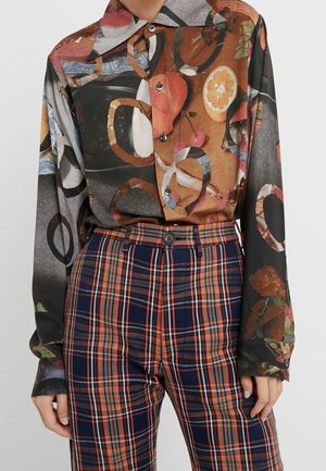 Koszula na guziki z długim rękawem, w brązowe, czarne i pomarańczowe owoce oraz wzór pierścieni, zestawiona z wysokim stanem granatowo-pomarańczowymi spodniami w kratę.