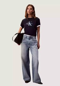 Maglietta nera a maniche corte con dettagli bianchi e logo "Calvin Klein", abbinata a jeans a gamba larga azzurri e borsa nera.