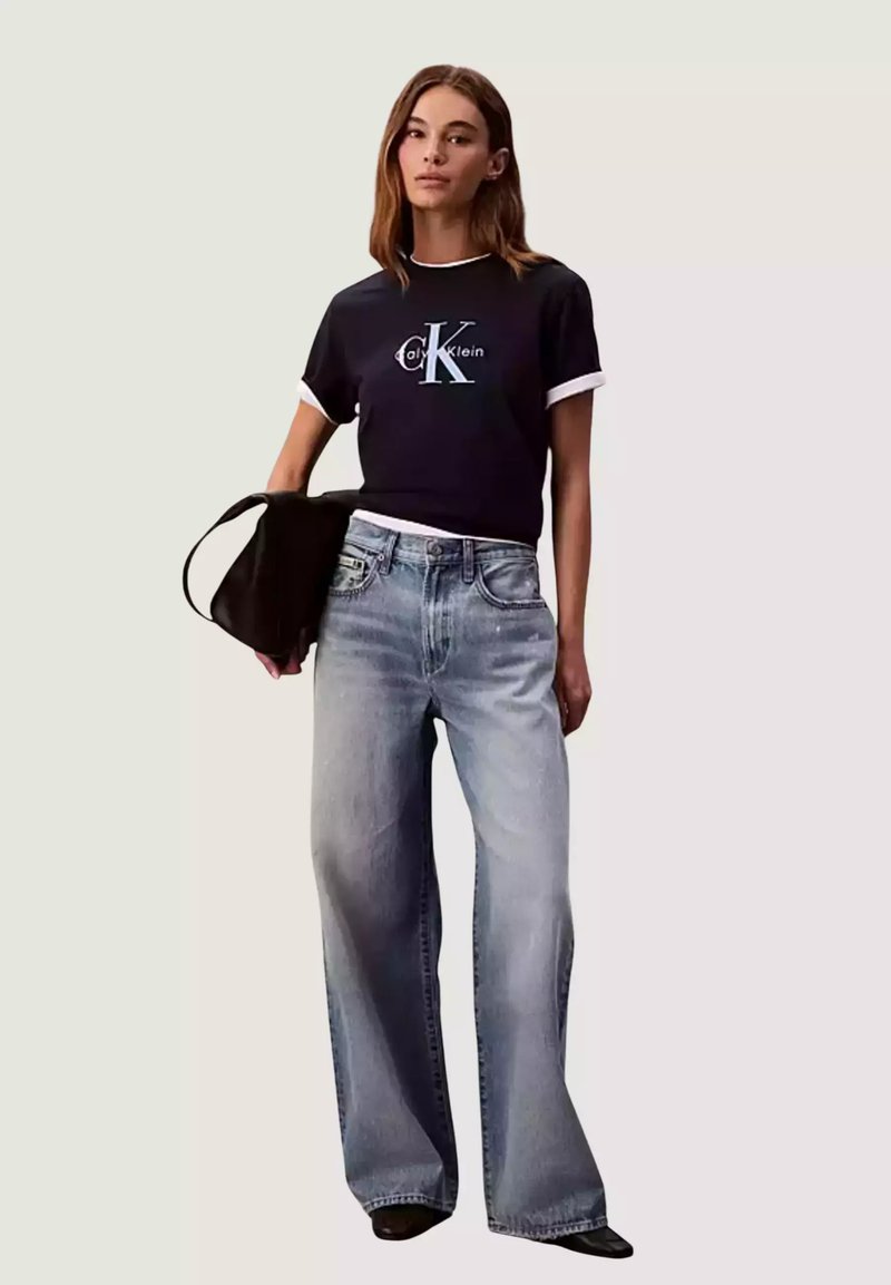 Maglietta nera a maniche corte con dettagli bianchi e logo "Calvin Klein", abbinata a jeans a gamba larga azzurri e borsa nera.