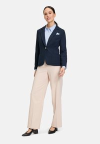 Granatowa marynarka z dwoma przednimi kieszeniami, beżowe spodnie z szerokimi nogawkami oraz jasnoniebieska koszula w paski. Czarne buty na obcasie z kwadratowym noskiem.