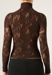 Top lungo a maniche lace marrone con collo alto, caratterizzato da motivi floreali intricati e un design aderente che esalta la silhouette.