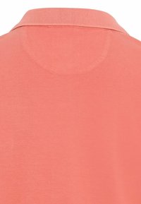 Polo en corail avec un col côtelé, texture lisse et un design de dos arrondi. Conçu pour une coupe près du corps.