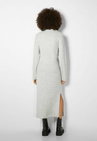 Harmaa neulemekko, jossa on pitkät hihat, korkea pääntie ja sivuventtiili; yhdistetty mustiin tukeviin saappaisiin. Pehmeä tekstuuri, nilkkapituinen muotoilu.