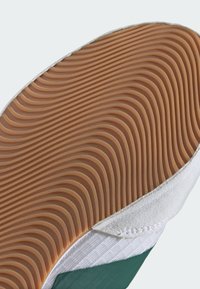 Tomaia in suede bianco con accenti verdi e motivo tessile diagonale. Suola in gomma con texture ondulata, colore tan. Dettagli di cucitura testurizzati.
