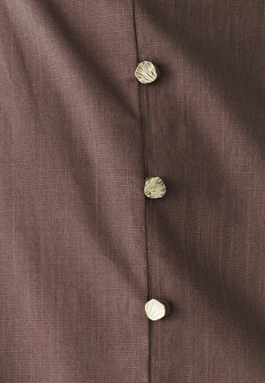 Brązowa tkanina o fakturowanej powierzchni z guzikiem w kształcie muszli w złotym odcieniu wzdłuż szwu. Widać cztery guziki, równomiernie rozmieszczone.