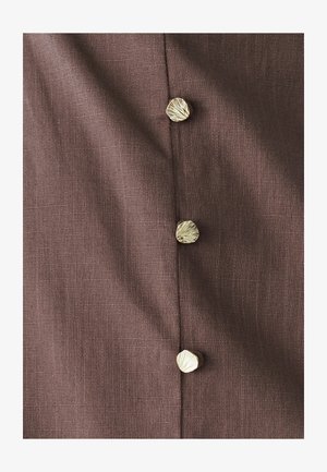 Brązowa tkanina o fakturowanej powierzchni z guzikiem w kształcie muszli w złotym odcieniu wzdłuż szwu. Widać cztery guziki, równomiernie rozmieszczone.