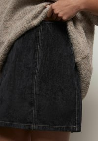 Jupe en denim noir avec une texture douce et des coutures visibles. Le tissu présente un aspect légèrement usé, complétant un pull en tricot beige.