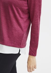 Top a maniche lunghe in tessuto bordeaux melange, con orlo bianco a strati e design aderente. Texture morbida con dettagli minimi.