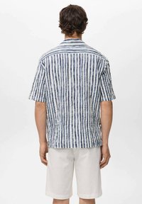 Korte mouwen shirt met verticale blauwe en witte strepen, textuurstof en een relaxte pasvorm, gecombineerd met lichte shorts.