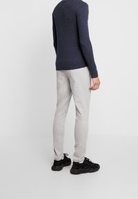 Granatowy sweter w prążki, szare dresy i czarne buty sportowe. Strój prezentuje luźny krój z teksturowanym materiałem oraz neutralnymi kolorami.