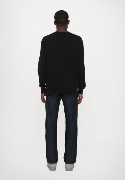 Schwarzer Sweatshirt mit gerippten Bündchen und Saum, kombiniert mit dunkelblauen, geraden Jeans und grauen Sneakers, von hinten betrachtet.