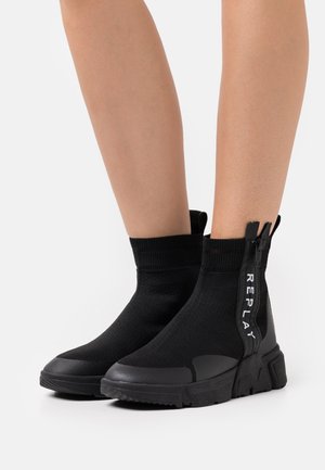 Schwarze sockenartige Ankle Boots mit einem Obermaterial aus strukturiertem Stoff, kontrastierender Gummisohle und einem seitlichen Reißverschluss mit "REPLAY"-Branding.
