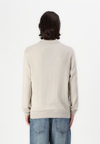 Beige long-sleeve sweater with a round neckline, ribbed cuffs, and hem, made from soft material; features a simple, textured design.