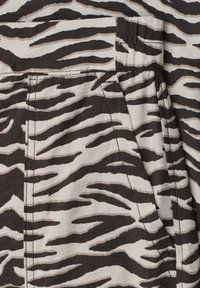 Gros plan sur un tissu avec des rayures zébrées noires et blanches et des coutures visibles bordant une poche sur un vêtement.