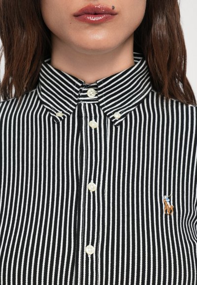 Chemise à rayures noires et blanches avec un col classique, dotée de boutons blancs et d'un petit logo brodé sur la poitrine.