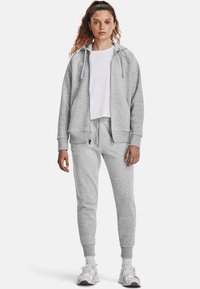 Gray hoodie with drawstrings, front pockets, paired with matching tapered sweatpants. Worn over a white t-shirt, featuring ribbed cuffs.