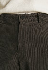 Bruna manchesterbyxor med vertikala räfflor, utrustade med knappstängning och midjeband. Texturerat tyg med mjuk finish.