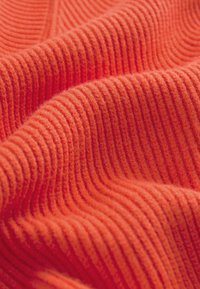 Texturerad, ribbad tyg i klar orange med mjuka, fluffiga fibrer, som visar svängande vågor och framträdande linjer i väven.