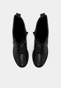 Pár černých kožených kotníkových bot na šněrování, pohled shora na bílém pozadí.