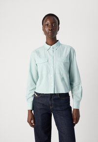 Ljusa blå randiga skjortan med två bröstfickor och en logotyp. Bärs med mörkblå jeans. Långa ärmar och klassisk kragsdesign.