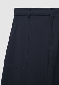 Marineblaue Hose mit glatter Textur, mit Fronttaschen, flachem Taillenbund und dezenten Nähdetails.