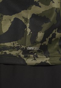 Primer plano de tela de camuflaje verde y negro con el texto "DRYCELL" impreso en blanco sobre un panel de tela negra.