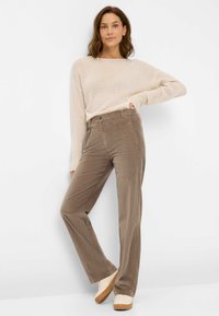 Beige trui gecombineerd met bruine corduroy broek. De broek heeft een recht model, voorzakken en een zachte textuur. Witte sneakers maken de look compleet.