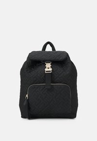 Sac à dos matelassé noir avec un motif géométrique, quincaillerie dorée, rabat supérieur et poche zippée à l'avant. La texture du tissu semble douce et durable.